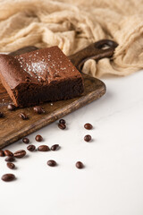 delicious brownie piece on wooden cutting board with coffee beans near cloth on white background