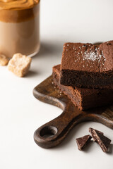 selective focus of delicious brownie pieces on wooden cutting board with chocolate near coffee in glass on white background
