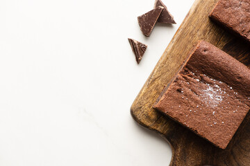 top view of delicious brownie pieces on wooden cutting board with chocolate on white background