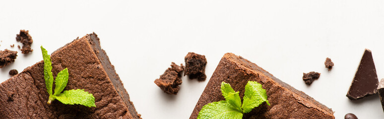 top view of delicious brownie pieces with mint and chocolate on white background, panoramic shot