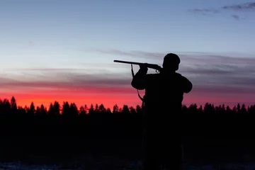 Rolgordijnen hunter aiming the hunting rifle during a hunt at sunrise © Александр Хализов