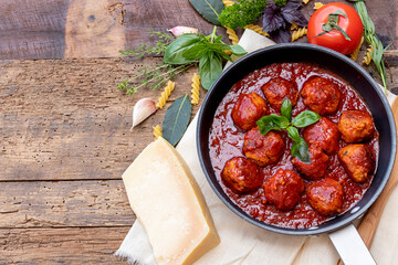 Top view of homemade meatballs with tomatoes sauce and herbs with basil leaves, cheese and garlic laydown on wooden background with copy space for text.