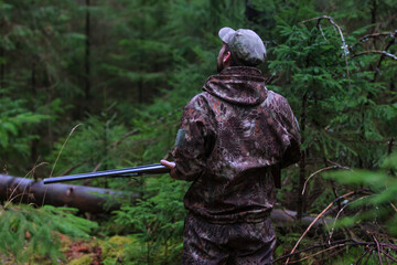 hunter in camouflage with shotgun walking in the forest