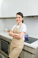 Portrait of young woman standing with arms crossed against kitchen background