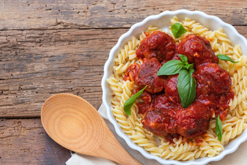 Top view of meatballs with fusilli Italian pizza with parmesan cheese, garlic, basil leaves and tomato on wooden background with natural color and copy space for text.