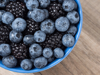 Forest berries (blueberry,bramble) in a ceramic blue  bowl. Top view. Space for text.