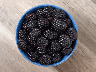 Ripe fresh blackberries in a bowl on a wooden table. Top view.