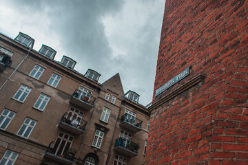 Fototapeta na wymiar Low angle view of signboard with name of street on brick facade of building and cloudy sky at background in Copenhagen, Denmark