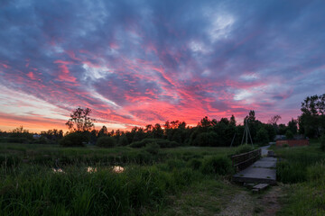 Naklejka na ściany i meble Beautiful landscape of nature with lovely sunset, small wooden bridge across a river and in the distance is green rice field
