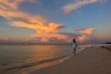 Fototapeta na wymiar woman walking on the beach near the ocean at the sunset