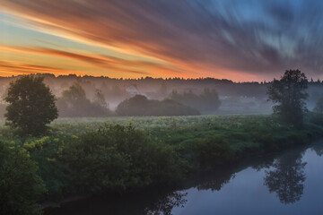 Foggy morning in the village. Colourful sunrise outdoors. Fantastic foggy river with fresh green grass