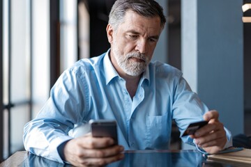 Fototapeta premium Online Payment on Smartphone by Mature Man. Handsome mature business leader sitting in a modern office