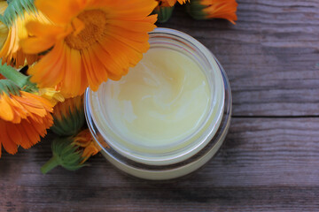 Obraz na płótnie Canvas Calendula flowers and diy face cream in glass jar on wooden table background with copy space. Homemade natural organic cosmetics with medicinal herbs.
