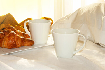 Morning coffee and croissants on a white bed. Romantic breakfast