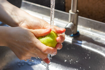 hands of woman washing a green apple in kitchen