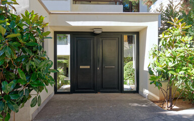 residential apartment buildinng enrtance metal and glass door by the sidewalk and green foliage