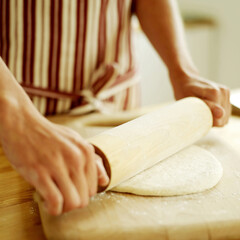 Chef rolling out pizza dough with a wooden rolling pin wearing a red stripy apron
