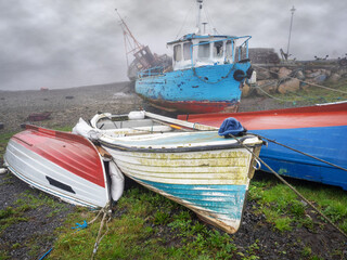 Old fishing boats on a ground at low tide in a fog. Fishing industry and equipment.
