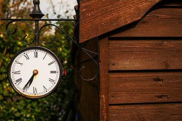 Old rusty retro style clock on a metal frame housing hanging on a side of a wooden barn, Green trees in the background out of focus. Concept time, and retro style in design.