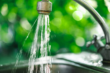 The flow of water from the tap with blurred background bokeh holiday season and the kitchen at the...