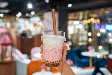 Rose bubble milk tea. Woman holding a plastic cup of rose tea with golden bubble/boba, topped with milk foam. (center)