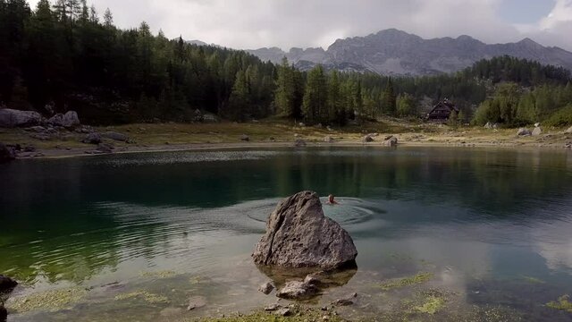 Aerial shot of handsome man jumping into the lake in the mountains, Triglav National Park, Slovenia