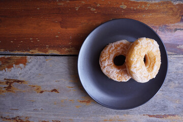 Donuts in a black ceramic plate on the old wood floor. Vintage background with copy space in Thailand.