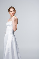 Fototapeta na wymiar beautiful woman in white wedding dress pointing with thumb isolated on grey
