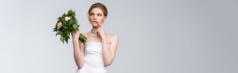 horizontal image of pensive girl in white wedding dress holding bouquet of flowers on grey
