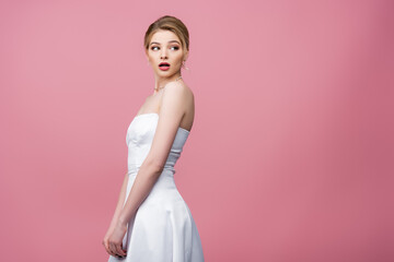 surprised bride in white wedding dress looking away isolated on pink