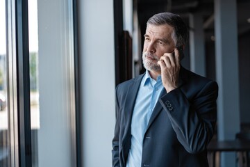 Senior business man talk on mobile phone at modern bright office interior.