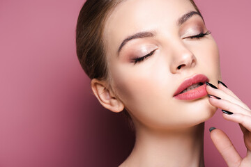 nude and pretty woman with closed eyes touching lips on pink
