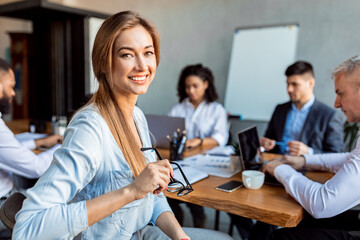Happy Businesswoman Looking At Camera Sitting With Colleagues In Office