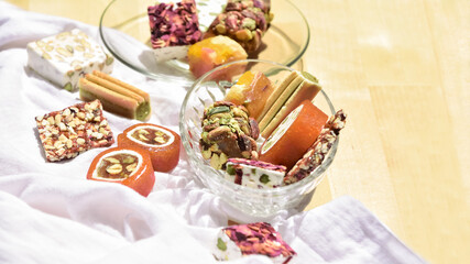 Fototapeta na wymiar Still life with different Lebanese sweets types (made from honeyed orange paste, dried fruits, roasted almonds, pistachios and rose petals) on a recycled wooden table covered with a white cloth