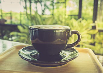 Wood table with cup of latte coffee in morning garden, side view.