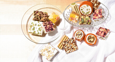 Still life with different Lebanese sweets types (with honeyed orange paste, dried fruits, roasted almonds, pistachios and rose petals) on a recycled wooden table covered with a white cloth. Top view