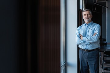 cheerful businessman with arms folded looking at the camera while standing near the window in office building.