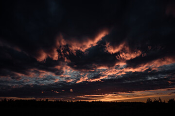 Gloomy dark clouds lit by the setting sun hung over the field and forest