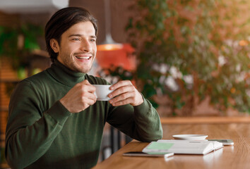 Enthusiastic guy freelancer having coffee break at cafe