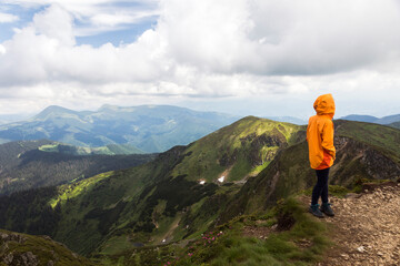 Tourist girl in orrange coat looks on the trail along the mountain range