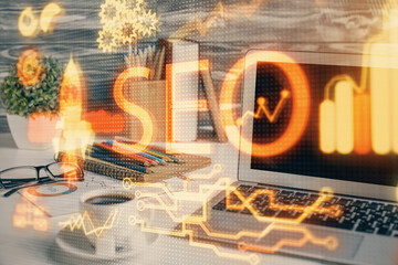 Double exposure of table with computer and seo drawing hologram. Search optimization concept.