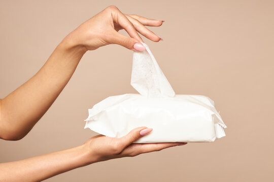Hygiene. Female hands takes wet wipes from white packaging on a beige background. Daily hygiene for the prevention of viral and bacterial infections.