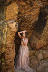 Sexy lady stand on rock in long dress. Beauty cute girl on a tropical beach sea ocean shore with large stones. Outdoor summer lifestyle.