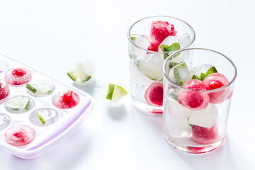 Cocktail glasses with berries in ice cubes on white table