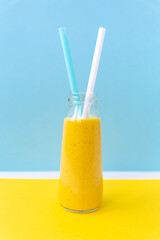 Smoothies, a mixed drink of milk, fruit and turmeric in a glass jar, straws for cocktails. Sky blue white yellow background. Minimalism, vertical, selective focus. Healthy nutrition, vegetarianism.