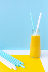 Smoothies, a mixed drink of milk, fruit and turmeric in a glass jar, straws for cocktails. Sky blue white yellow background. Minimalism, vertical, selective focus. Healthy nutrition, vegetarianism.