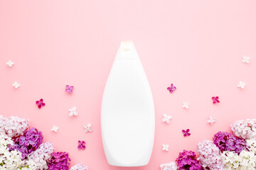 White bottle with colorful lilac on pastel pink table background. Care about clean and soft face, hands, legs and body skin. Women beauty product. Empty place for text or logo. Top down view. Closeup.