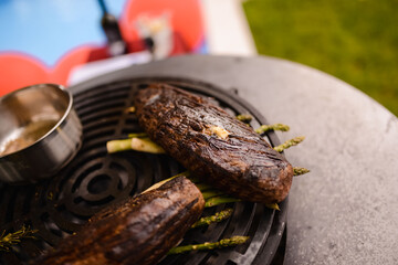 The chef grills steak and asparagus on the grill in the yard