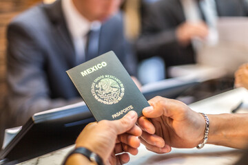 Las manos de una persona sostienen un pasaporte mexicano mientras hace el chek in en un hotel - obrazy, fototapety, plakaty