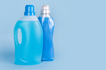 Bottles of detergent and fabric softener on blue background. Containers of cleaning products, household chemicals. Liquid laundry detergent and conditioner. Laundry day, washing and cleaning concept.